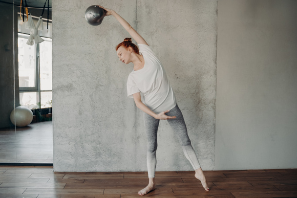 Red haired beautiful woman with fitball performing barre exercises - 写真・画像