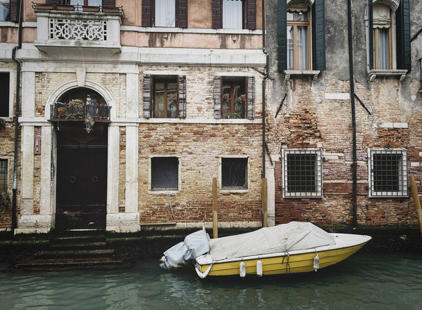 Vista lateral de un barco amarillo atracando frente a una antigua casa veneciana de ladrillos rojos - Foto, Imagen
