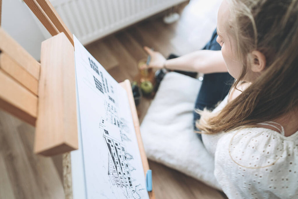 Top view of a young female student in a modern interior.Draws a sketch for an architectural project, uses a pencil and an easel.The concept of homeschooling and education during a pandemic.COVID-19 - Zdjęcie, obraz