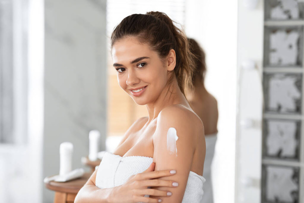 Giovane signora applicando crema sulla spalla idratante pelle in bagno - Foto, immagini