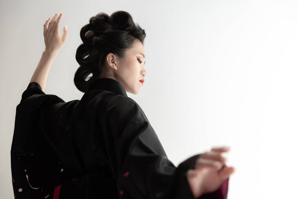 Portret młodej, pięknej Japonki, kobiety w narodowym stroju kimono pozującej na białym tle pracowni. - Zdjęcie, obraz