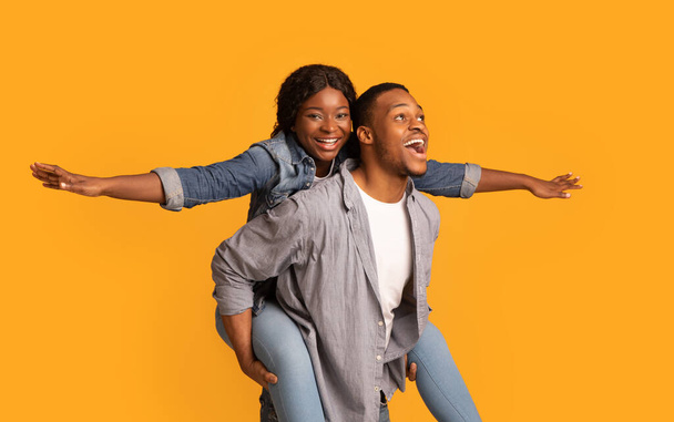 Gioioso nero coppia having divertimento insieme su giallo sfondo, donna piggybacking fidanzato - Foto, immagini
