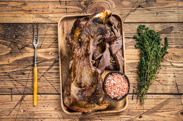 Roasted lamb mutton cutting shoulder meat in a wooden tray with meat fork. wooden background. Top view - Photo, Image