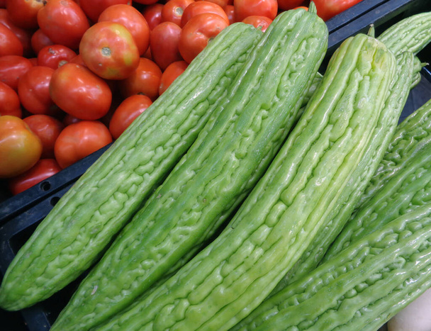 Pile of Vibrant Green Bitter Cucumber or Balsam Pear with Basket of Tomatoes in the Backdrop - Photo, Image