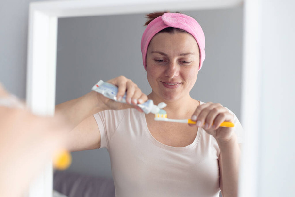 Feliz sorriso mulher escovação dentes espremendo creme dental de hortelã na escova de dentes de plástico, tomando cuidado com a respiração fresca e prevenção de cárie. - Foto, Imagem