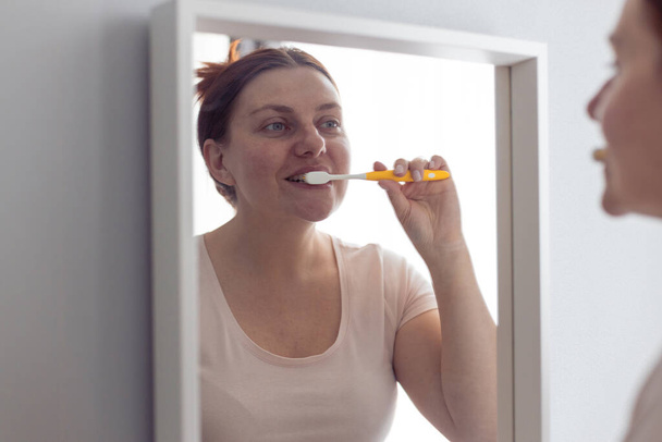 Portré gyönyörű Y-generációs nő fogmosás tükörben reggeli higiéniai eljárások a fürdőszobában. Higiénia, fogápolás. - Fotó, kép