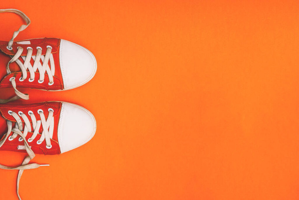 Молодіжні кросівки на помаранчевому тлі з копіювальним простором. Червоні кросівки з вільними шнурками. Мінімальний стиль. Вид зверху, плоский ліжко
 - Фото, зображення