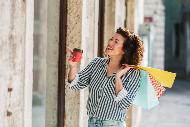Młoda kobieta spaceruje na zewnątrz z filiżanką kawy i torbami na zakupy po zakupach - Zdjęcie, obraz