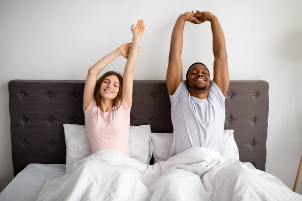 Giovane coppia interrazziale che si estende sul letto dopo il risveglio al mattino, al chiuso - Foto, immagini
