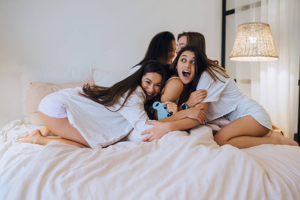Positive young girls women friends indoors on bed at the hen party at home. - 写真・画像