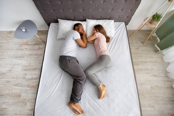 A szeretetteljes multiracionális pár teljes hossza együtt alszik az ágyon, egymással szemben, felülnézetből - Fotó, kép