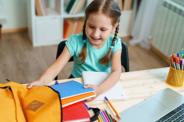 Cute happy schoolgirl puts office supplies in a backpack. Preparation for school. Back to school. Self-Assembly of a school backpack. - Fotoğraf, Görsel