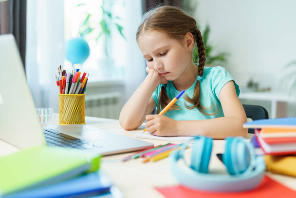 little girl is tired of learning. home schooling, homework. girl rubs his eyes from fatigue reading books and textbooks. little kid student sitting at table with books. vision problems - Photo, image