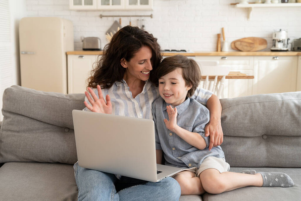 Anne ve küçük çocuk, dizüstü bilgisayardan babalarına gülümseyen bilgisayar kameralarına selam veriyorlar. - Fotoğraf, Görsel
