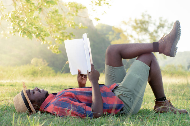 African man reading a book on the grass happily on vacation - Фото, зображення