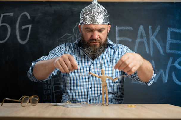 a distraught schizophrenic conspiracy theorist in a protective foil cap controls a man - a toy. Consciousness manipulation. Conspiracy theory. Mind control. - Photo, Image