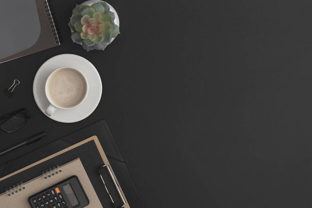 電卓、ノートブック、コーヒーカップと緑の植物とブラックレザーオフィステーブル。コピースペース付きのトップビュー。平面構成. - 写真・画像