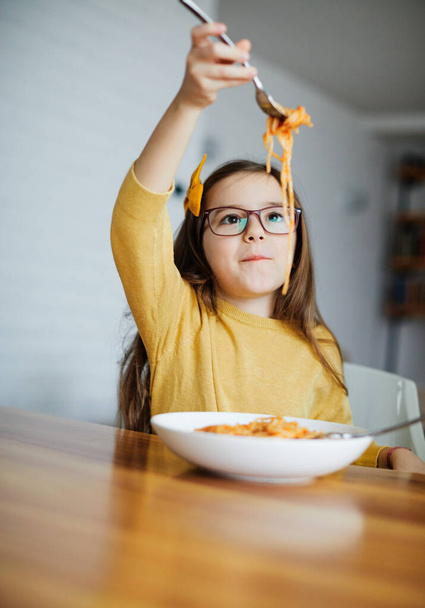 gelukkig klein meisje eten spaghetti thuis - Foto, afbeelding