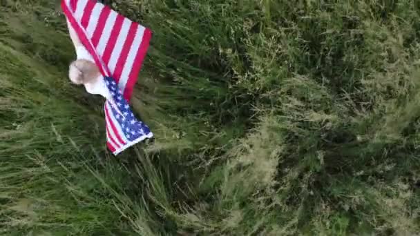 Buğday tarlasında gün batımında Amerikan bayrağıyla kaplanmış Amerikalı bir kadın. - Video, Çekim