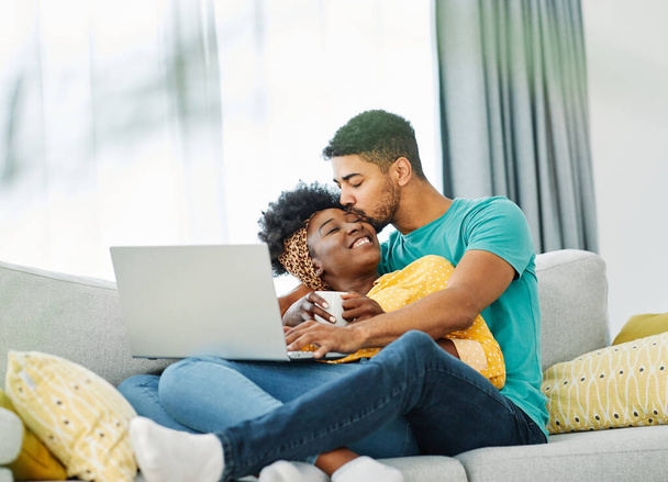 Retrato de una encantadora pareja joven juntos sosteniendo el ordenador portátil en el sofá en casa - Foto, imagen