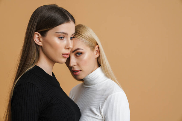 Beautiful two women posing head to head on camera isolated beige background - 写真・画像