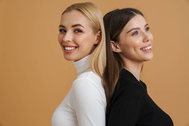 Beautiful smiling women posing back to back on camera isolated beige background - Foto, immagini