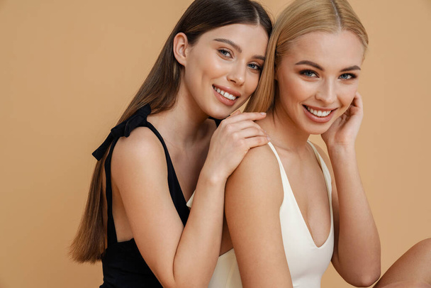 Happy two women wearing swimsuits hugging and smiling at camera isolated beige background - Photo, Image