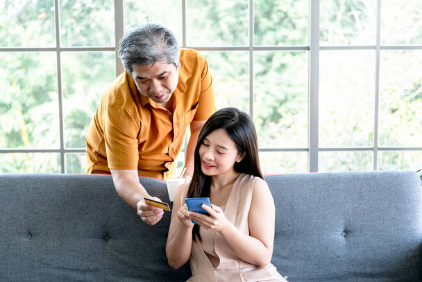 Asian couple, attractive wife Using mobile phones and looking at mock up credit card, which her husband holds for shopping online, to business and shopping online concept. - Photo, image