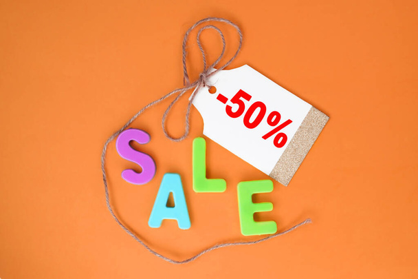 The word sale is written in plastic multicolored letters on an orange background. A tag for the price tag with the inscription minus fifty percent - Foto, Imagem