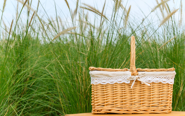 公園内の小さな木製のテーブルの上に木製のピクニックバスケットを織った。夏の晴れた日とピクニックの時間のコンセプト - 写真・画像