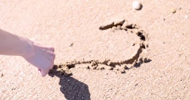 Kobieta rysuje serce palcem na mokrej plaży piasek 4k film - Materiał filmowy, wideo