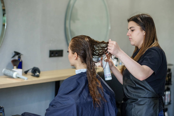 Ein Mädchen im Schönheitssalon, ein Friseur frisiert ihr Haar, schneidet ihr Haar zu einem Mädchen mit langen Haaren. - Foto, Bild