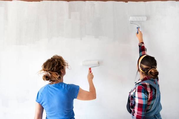 Dos mujeres pintando nuevas paredes de apartamentos en color blanco con rodillo de pintura. Renovando el hogar. Concepto inmobiliario. Copiar espacio - Foto, Imagen