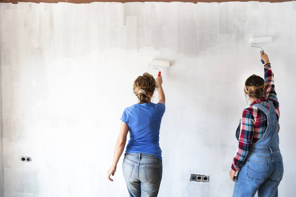 Dwie kobiety malujące nowe ściany mieszkalne w kolorze białym z wałkiem malarskim. Odnawiam dom. Koncepcja nieruchomości. Przestrzeń kopiowania. - Zdjęcie, obraz