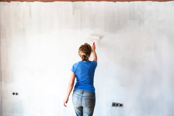 Femme peignant de nouveaux murs d'appartement en couleur blanche avec rouleau de peinture. Rénovation de la maison. Concept immobilier. Espace de copie - Photo, image