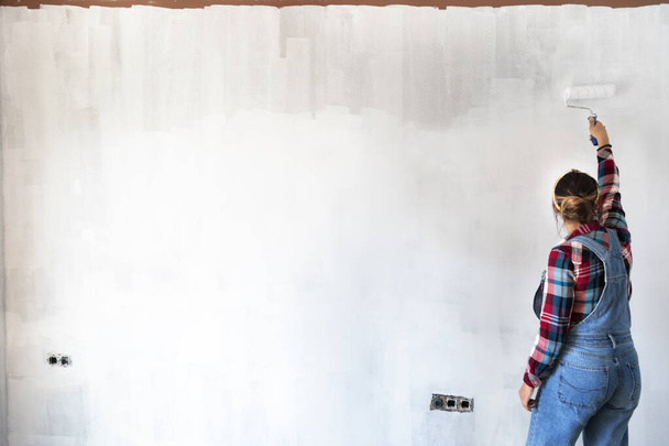 Νεαρή γυναίκα ζωγραφίζει νέους τοίχους διαμερισμάτων σε λευκό χρώμα. Ανακαινίζω το σπίτι. Σχέδιο ακίνητης περιουσίας. Αντιγραφή χώρου - Φωτογραφία, εικόνα