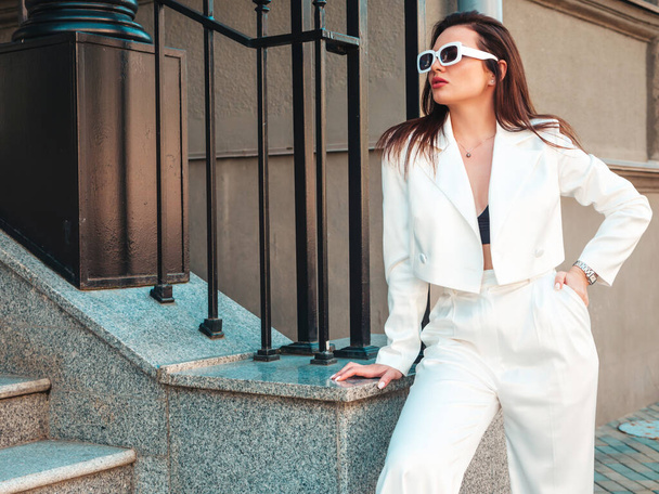 Portrait of young sexy modern businesswoman model. Hot beautiful woman in white suit posing on the street background. Fashion female outdoors in sunglasses - Photo, image