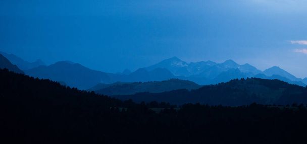 Mavi saatte panoramik dağ katmanları. Alp dağlarının koyu mavi sisli siluetleri ve Pireneler 'deki köknar ağaçları ormanlarıyla manzara. - Fotoğraf, Görsel