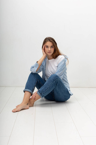 young caucasian pretty girl with long hair in shirt, blue jeans sits at studio - Fotografie, Obrázek