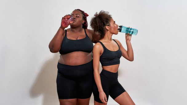 Couple of afro women drinking from sport-bottles, self acceptance concept  - Fotografie, Obrázek