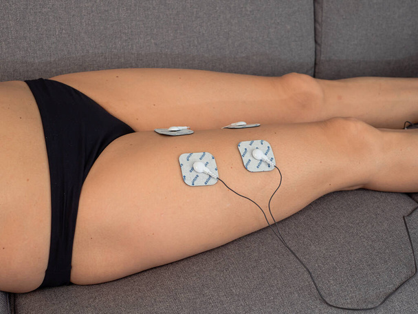 Mujer en terapia con electrodos colocados en las piernas, rehabilitación postraumática - Foto, Imagen