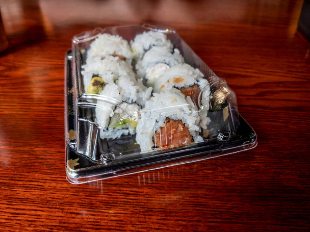 Vista inclinada de um recipiente de levar preto cheio de sushi em uma mesa de madeira brilhante em um restaurante - Foto, Imagem
