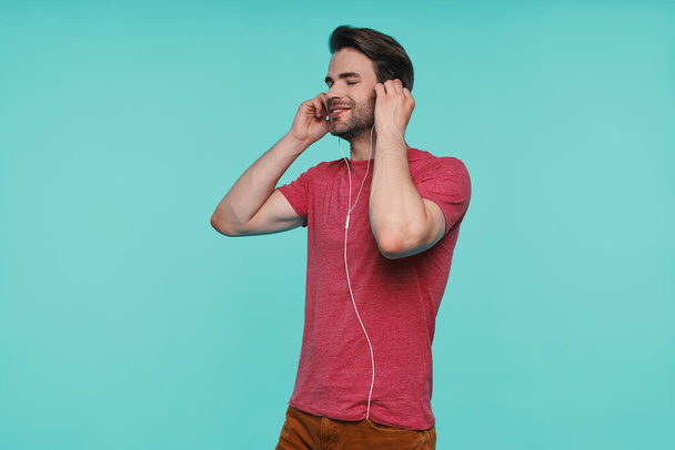 Handsome young man in headphones keeping eyes closed and smiling - Zdjęcie, obraz