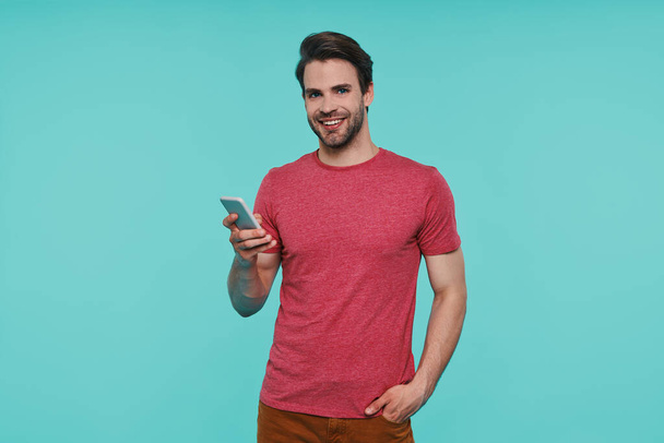 Handsome young smiling man in casual clothing holding smart phone - Fotoğraf, Görsel