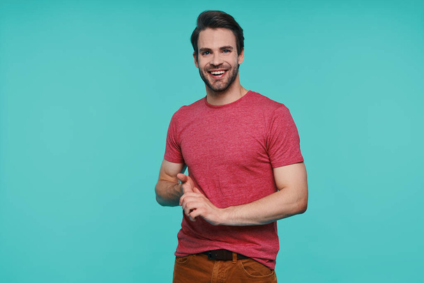 Handsome young man in casual clothing looking at camera and smiling while standing against blue background - Fotoğraf, Görsel