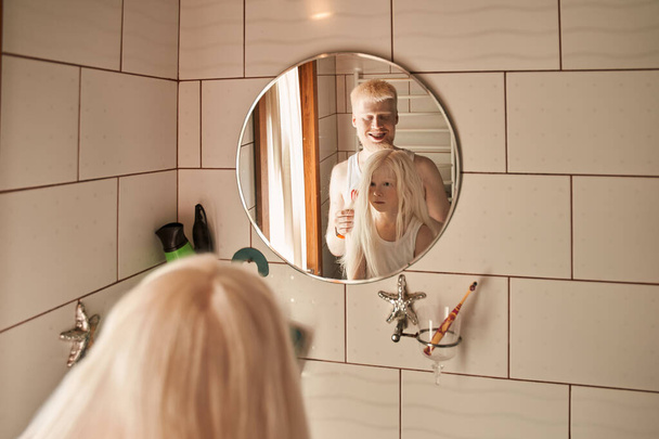 Man doing hairstyle for his little daughter at the bathroom while smiling - Valokuva, kuva