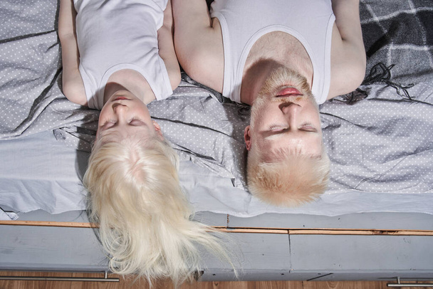 Girl laying at the bed with closed eyes near her bearded albino father and relaxing - Valokuva, kuva