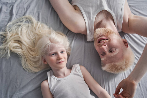 Girl laying at the grey blanket with her albino father while spending time at home - Valokuva, kuva