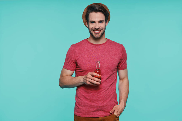 Handsome young man in casual clothing holding bottle with drink and smiling - Fotografie, Obrázek