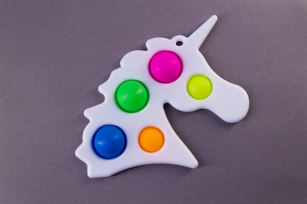 Juguete colorido brillante Simple Dimple unicornio. Popular juguete anti estrés sobre fondo gris - Foto, imagen